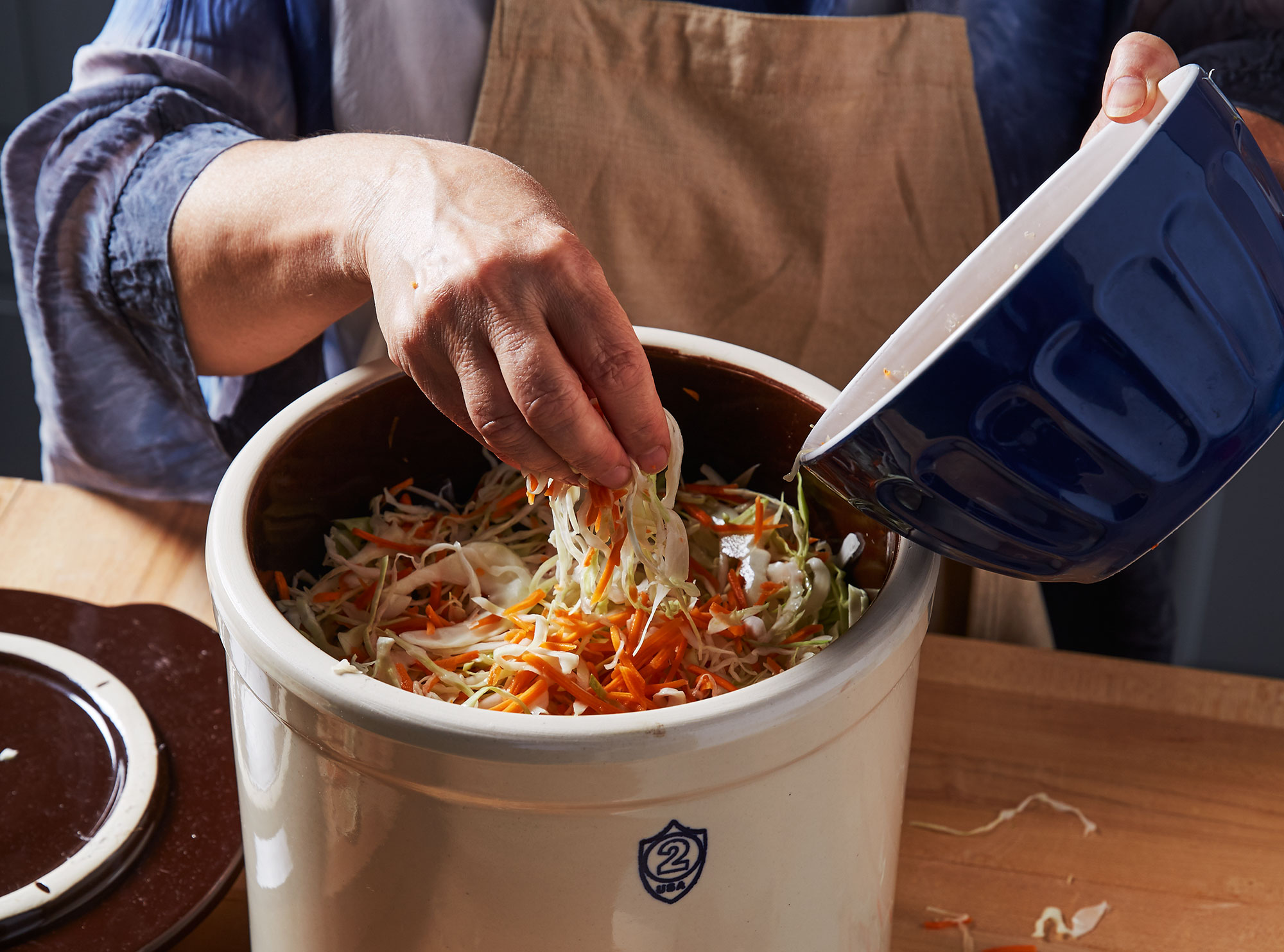 Transferring sauerkraut ingredients from a bowl into a fermentation crock