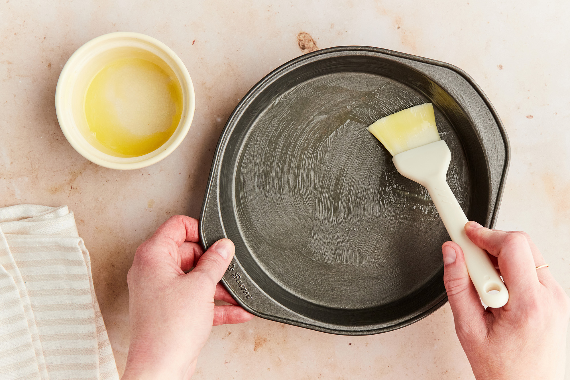 Using a pastry brush to grease a baking pan with melted butter.
