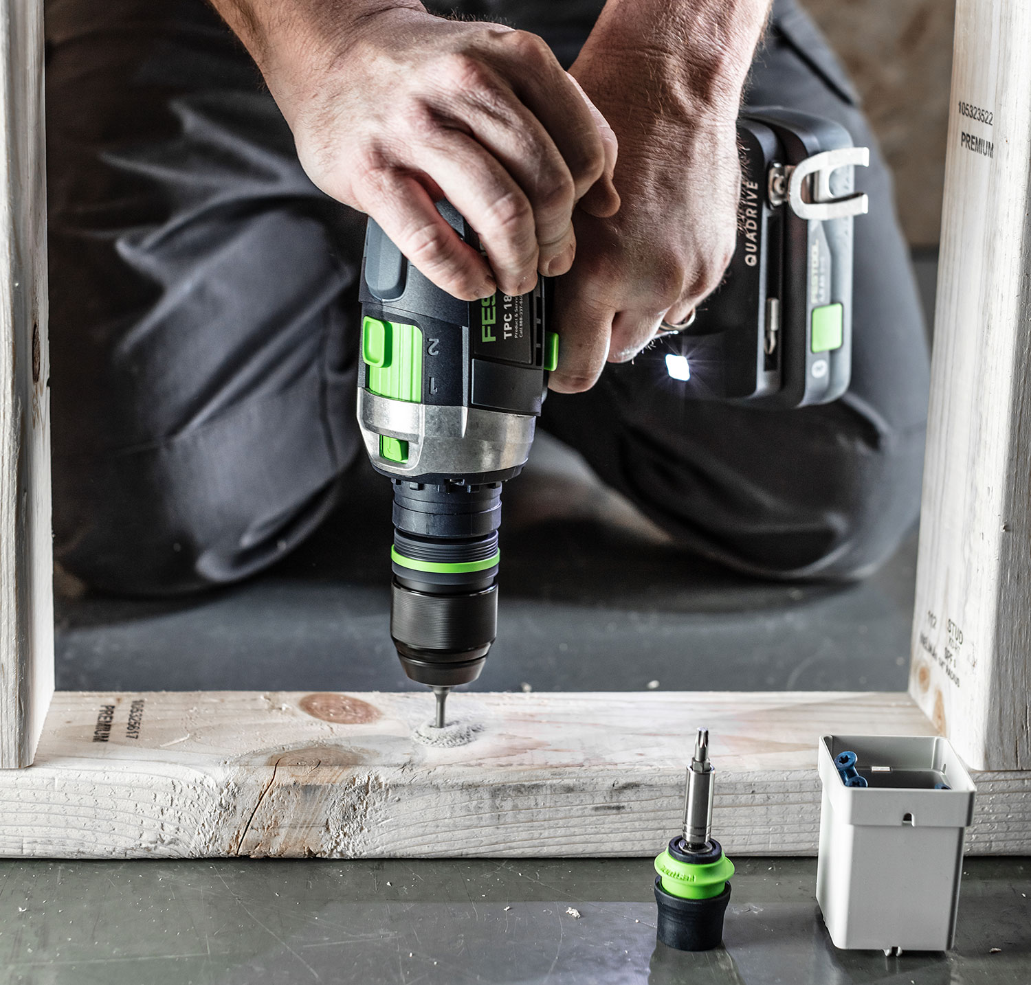 A carpenter using a Festool 18-volt drill on the bottom plate of a wall