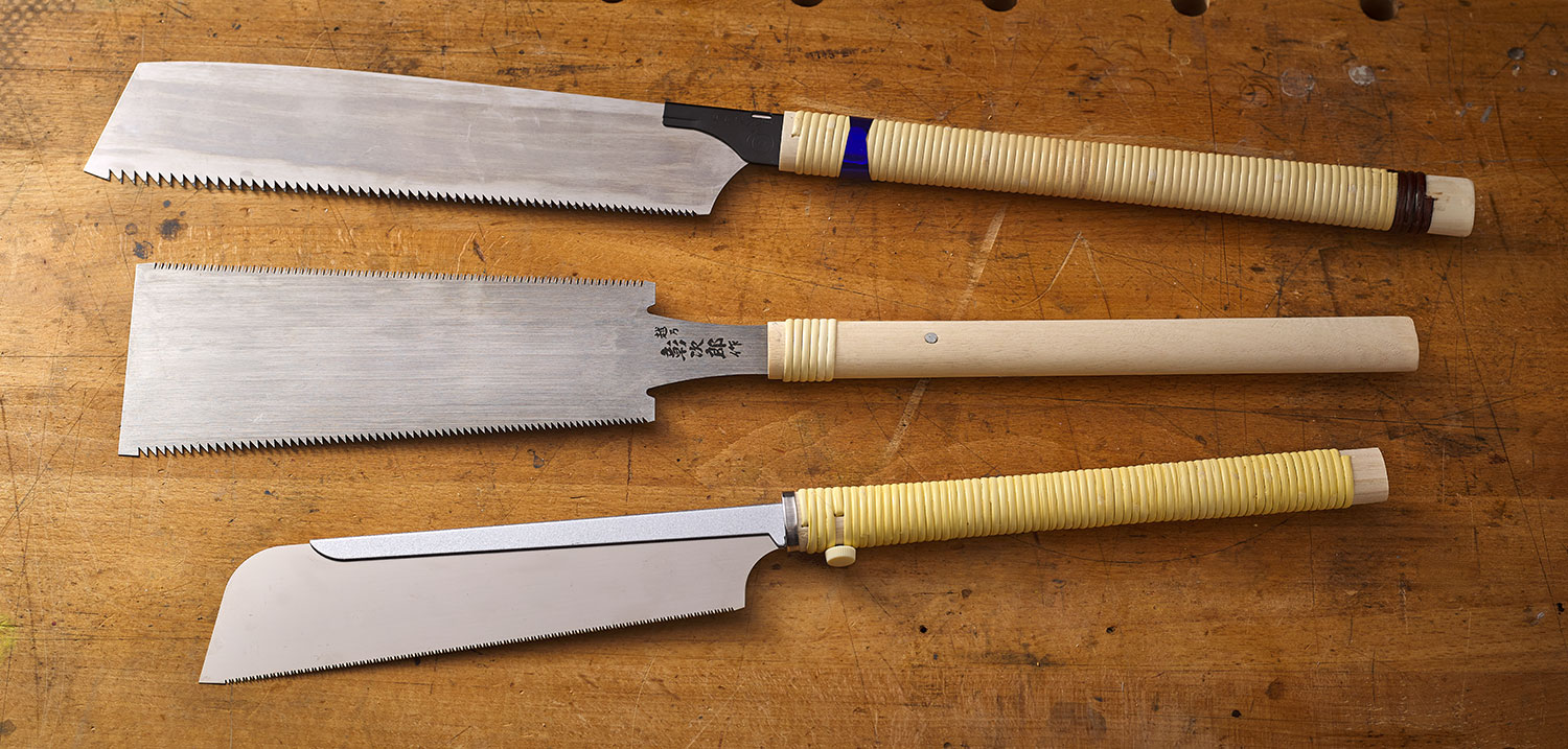 Three different styles of Japanese saws, kataba, ryoba, and dozuki, sitting on a workbench.
