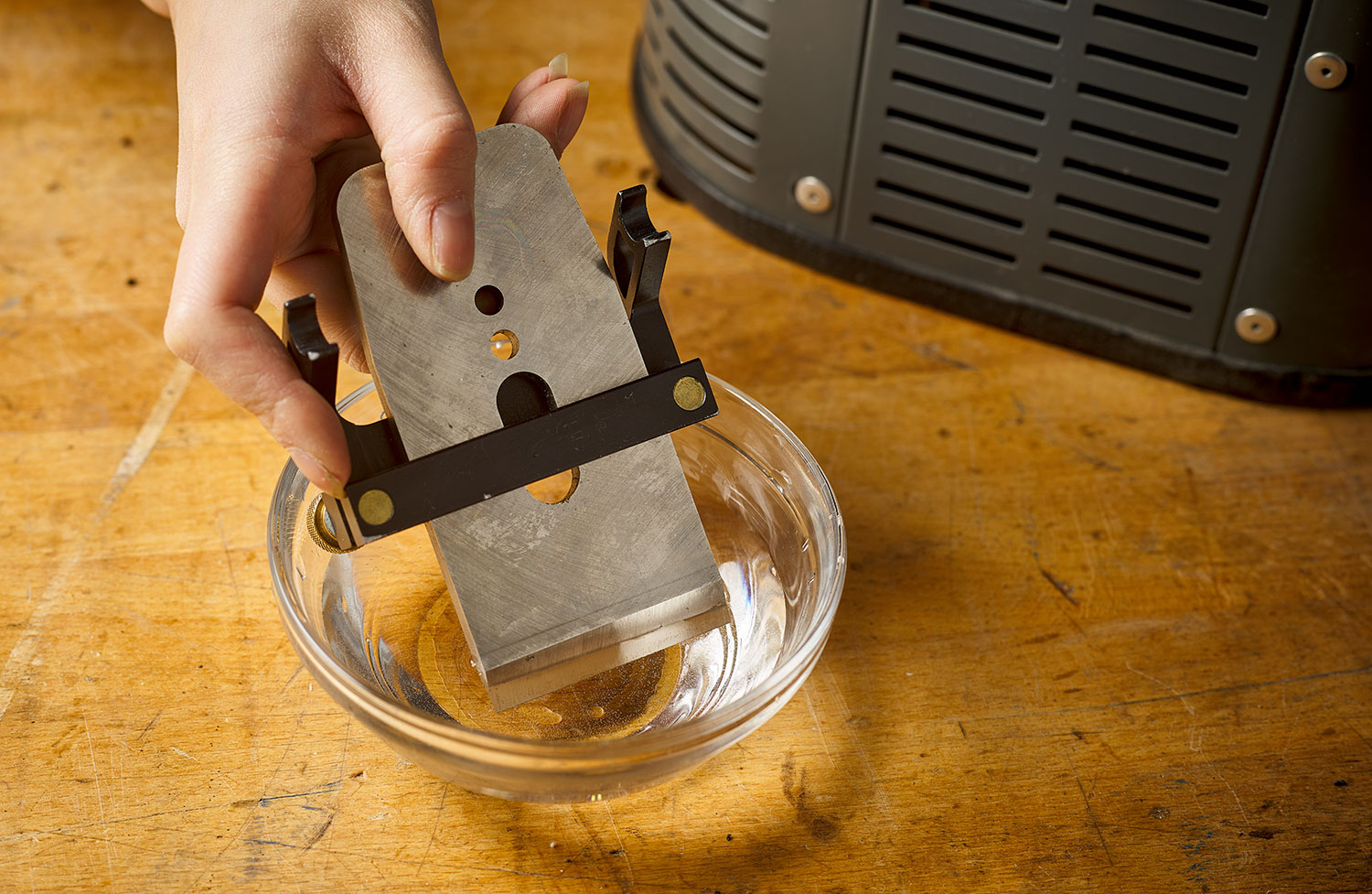 A woodworker dips a plane blade in a dish of water to cool it after grinding the primary bevel.
