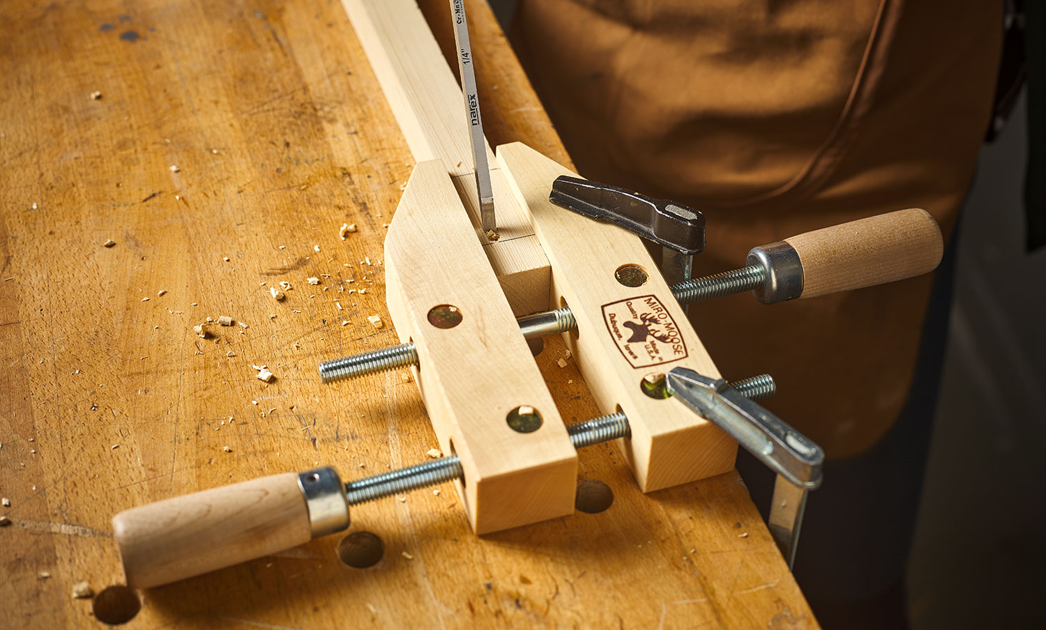 A board is held in a clamp while a Narex chisel is being used to cut a mortise.