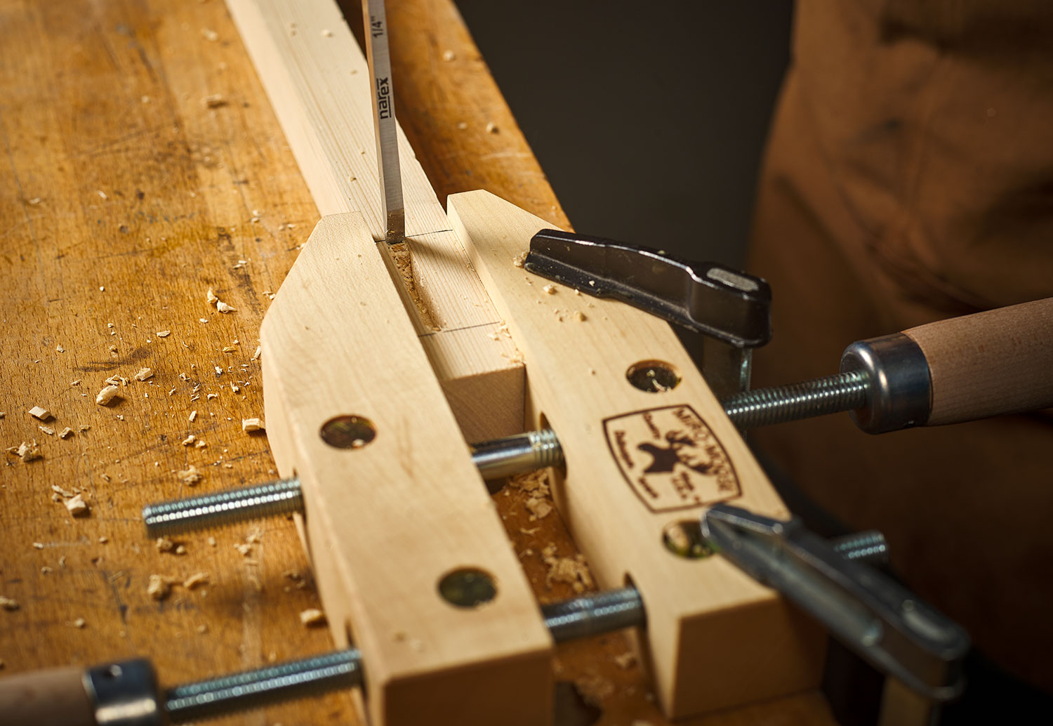 A Narex mortise chisel is being used to cut a mortise on a board in a clamp.