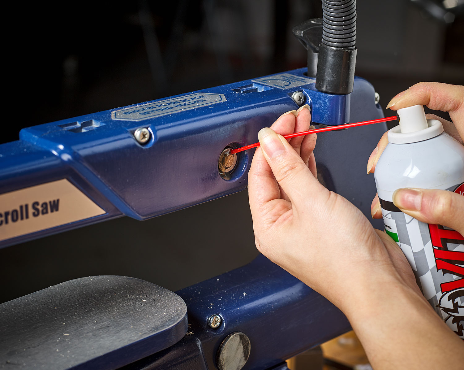 A woodworker lubricates the saw arm bearings on a 16-inch scroll saw