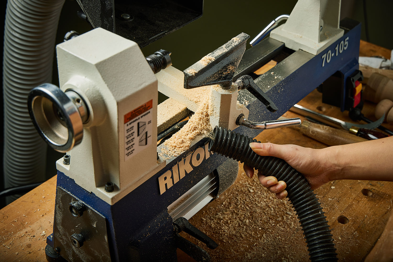 A turner uses a vacuum hose to collect accumulated wood shavings from the bed rails of a Rikon lathe