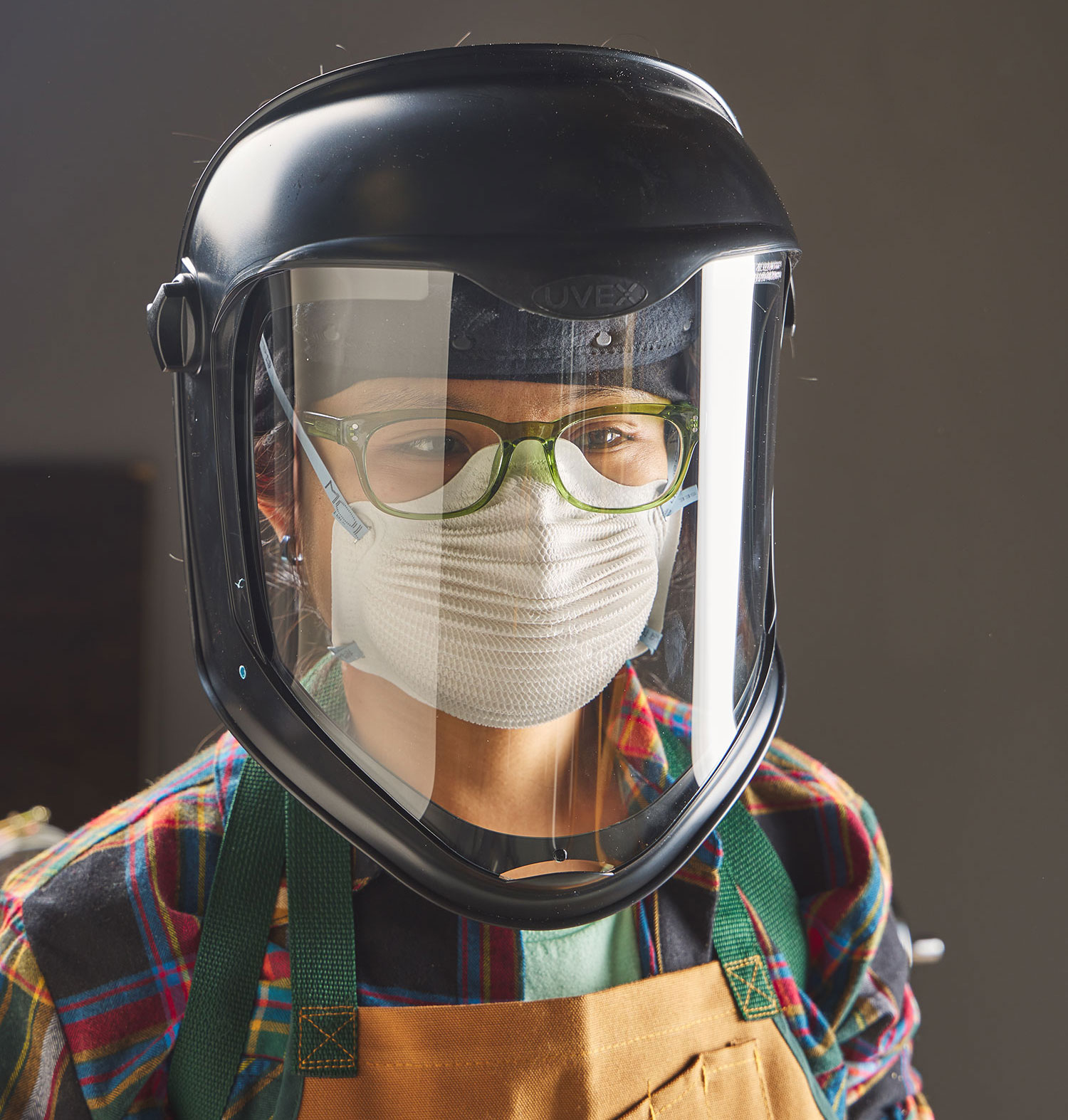 A turner wearing a face shield, dust mask and canvas apron for protection when working on a lathe