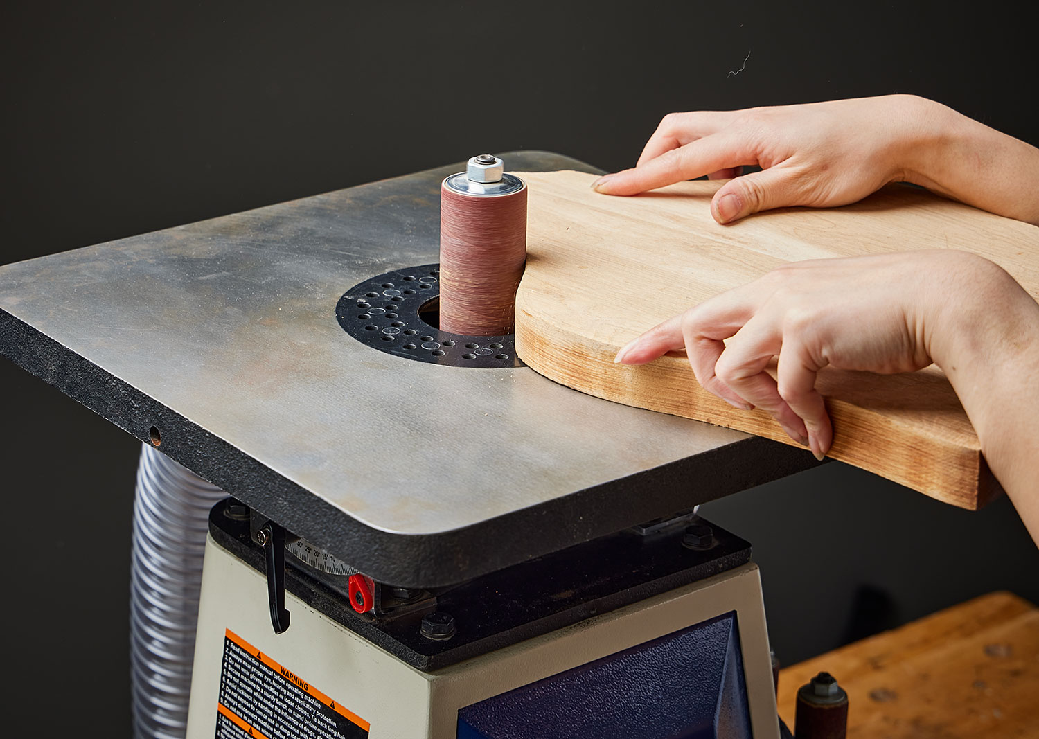 A woodworker uses a Rikon spindle sander to smooth the edge of a wooden workpiece.