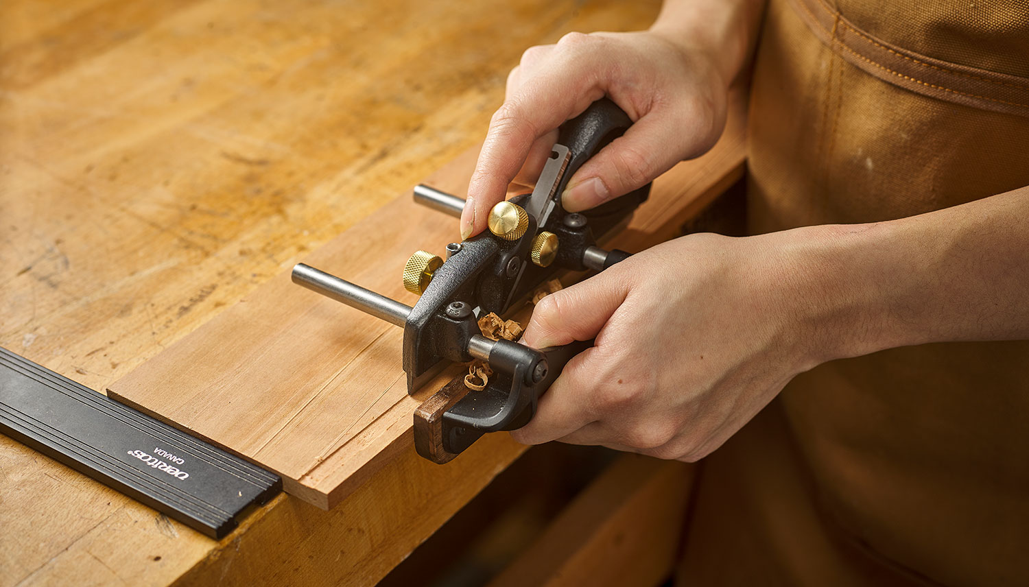 Using a box-maker’s plow plane to cut a groove in the wall of a wooden box to hold the box bottom.