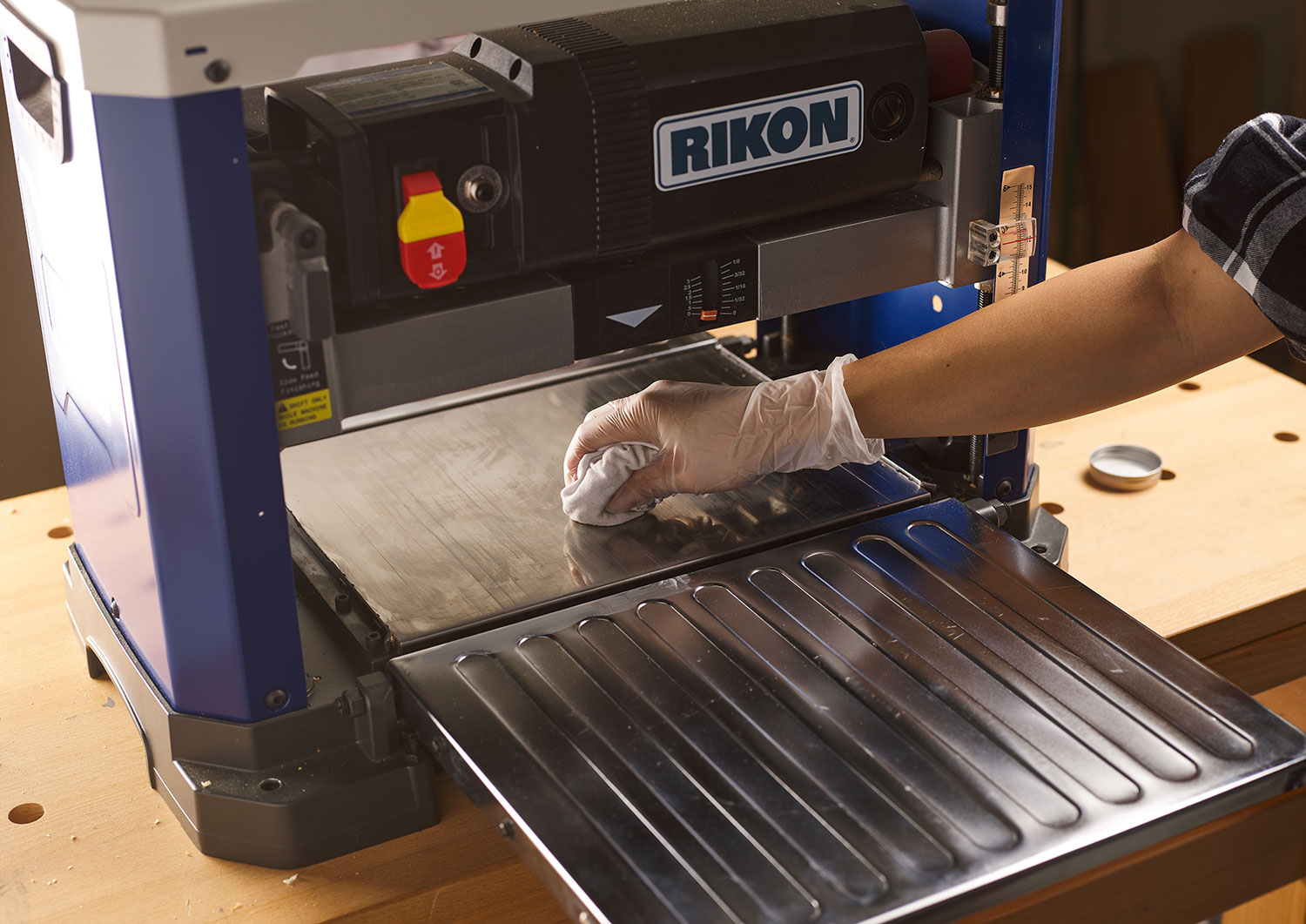 The bed of a Rikon helical planer is being wiped with a white cloth.
