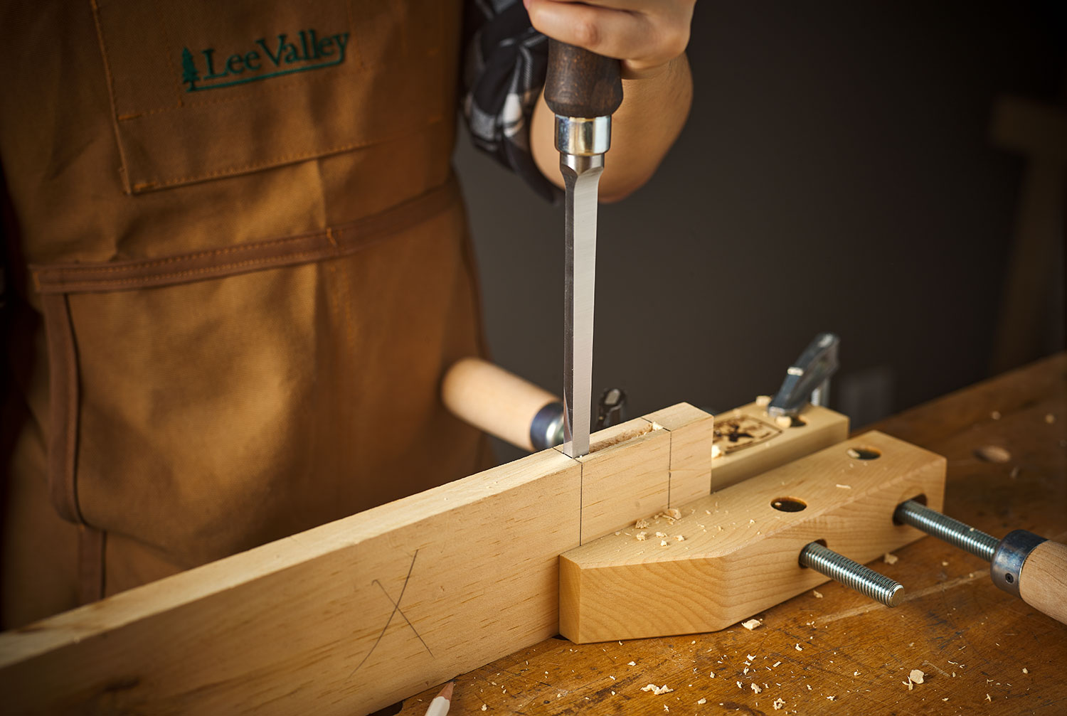 A Narex chisel is being held at a 90° angle to cut a mortise into a board.