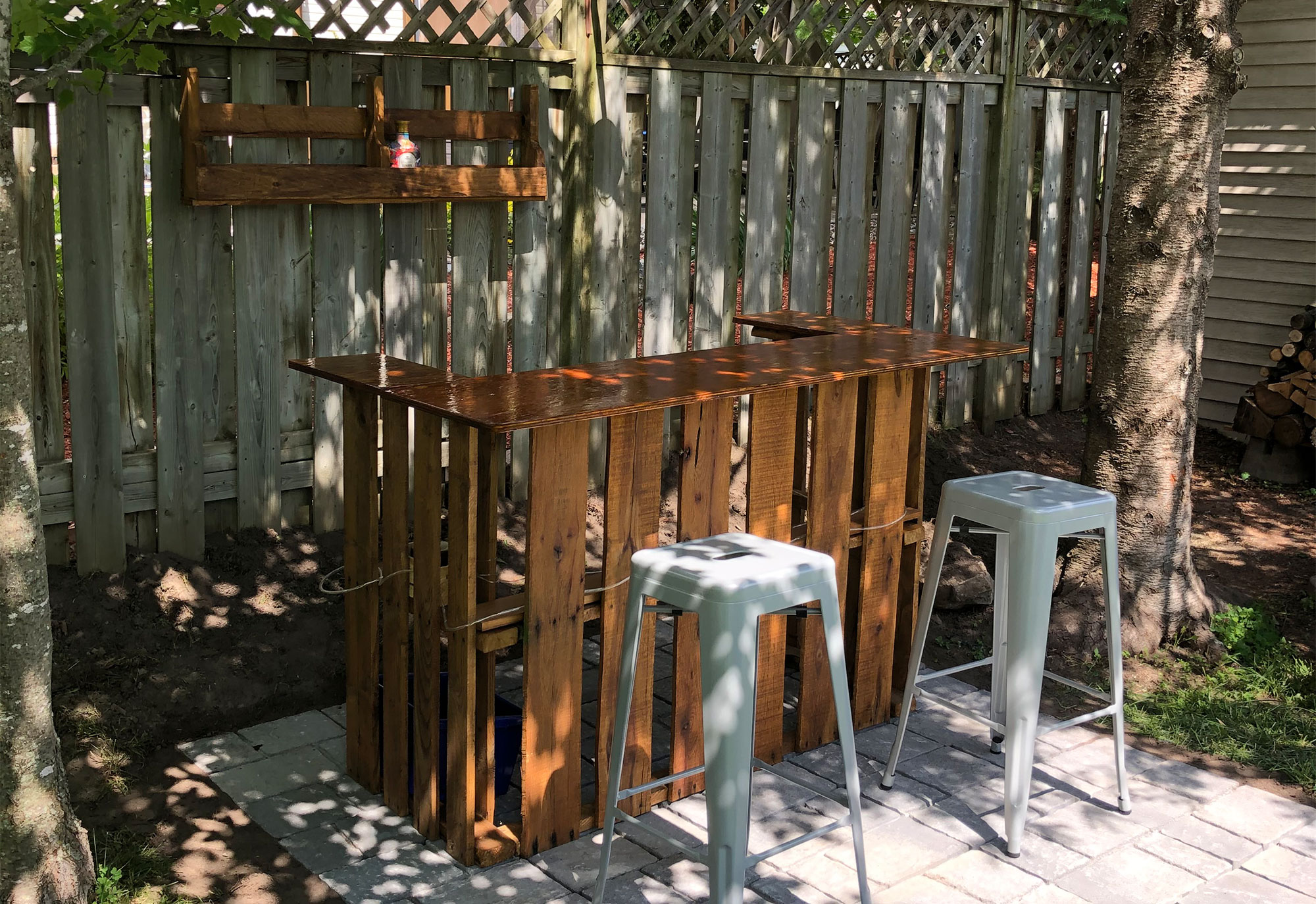 Make a Backyard Bar Using Pallets. Backyard bar made out of pallets with two bar stools in front of it.