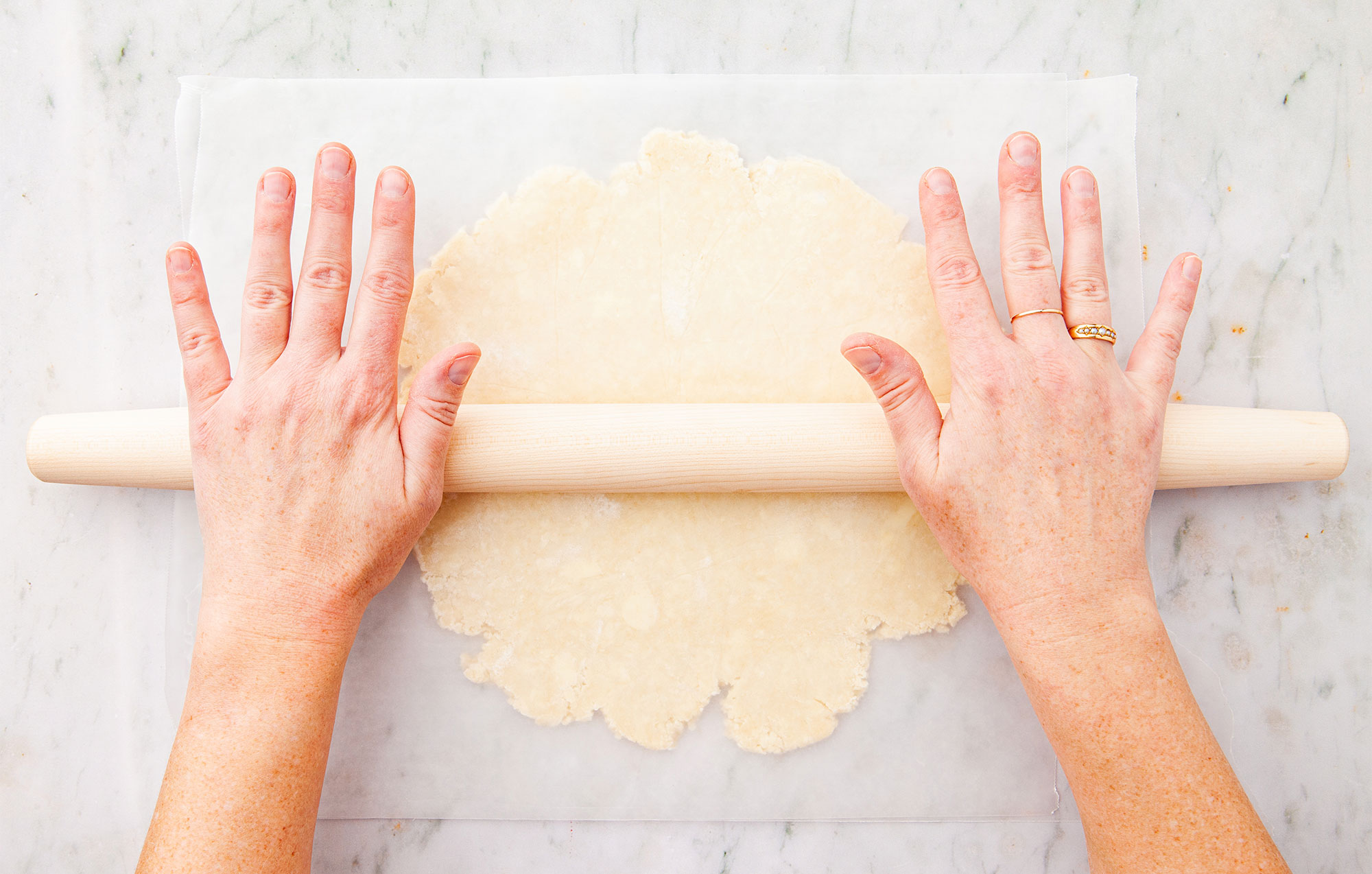 Deux mains pressant un rouleau à pâte en érable sur une abaisse de pâte